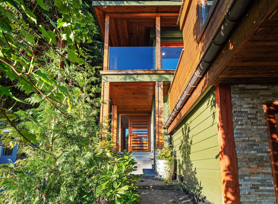 Experience modern living in this stunning home featuring a sleek wooden exterior and a welcoming entryway with a glass-paneled door.