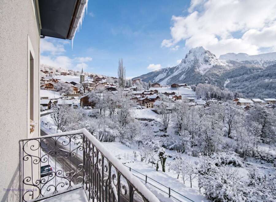 Experience the magic of a winter wonderland from your private balcony, offering breathtaking panoramic views of a snow-covered village nestled in the Alps.