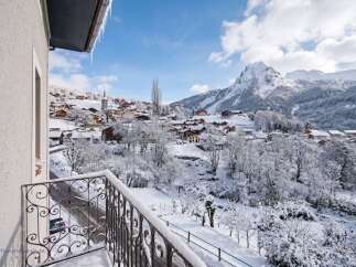 Experience the magic of a winter wonderland from your private balcony, offering breathtaking panoramic views of a snow-covered village nestled in the Alps.