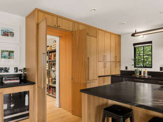 Discover this stunning modern kitchen featuring custom light wood cabinetry that seamlessly integrates a hidden pantry.
