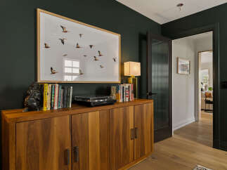 This inviting hallway features a dark green accent wall adorned with a large framed print of flying birds, creating a striking focal point.