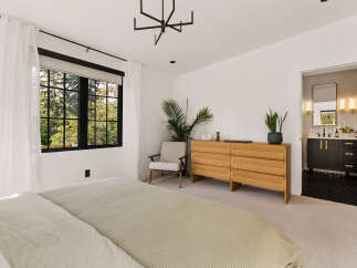 Experience modern comfort in this serene bedroom, featuring a plush bed, a stylish accent chair, and a sleek wooden dresser.