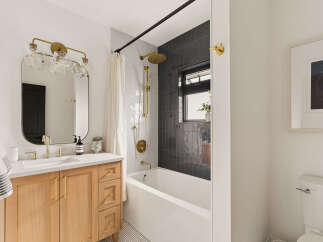 This modern bathroom features a sleek wooden vanity with gold hardware, complemented by a minimalist white countertop and sink.