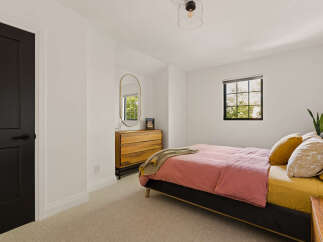 This inviting bedroom features a comfortable bed with a pink duvet and accent pillows, complemented by a wooden dresser and an oval mirror.