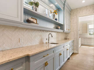 This stunning kitchen features elegant light blue cabinetry with ornate gold hardware, complemented by a beautiful herringbone tile backsplash and a speckled granite countertop.