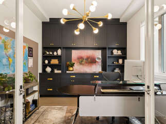 This modern home office features a sleek dark cabinetry system with gold hardware, complemented by a vibrant abstract painting and a stylish gold sputnik chandelier.