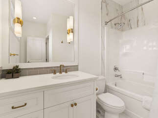 This modern bathroom features a sleek white vanity with brass hardware, complemented by a marble-tiled shower and tub surround.