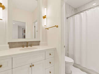 This elegant bathroom features a white vanity with brass hardware and a quartz countertop, complemented by a grey subway tile backsplash.