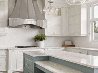 This stunning kitchen features a large, modern stainless steel range hood as the centerpiece, complemented by elegant white cabinetry and a herringbone tile backsplash.