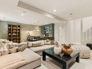 This spacious basement living area features a large sectional sofa, a stylish coffee table with decorative vases, and a built-in bar with green cabinetry.