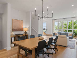 Experience modern living in this open-concept dining and living area, featuring a sleek black chandelier and a warm wooden dining table with black chairs.