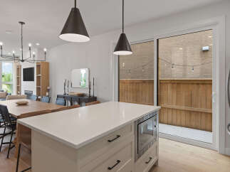 This modern open-concept dining and kitchen area features a large wooden dining table with upholstered chairs, complemented by a sleek white kitchen island with integrated microwave.
