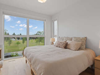 Experience modern comfort in this serene bedroom, featuring a large window that floods the space with natural light and offers picturesque views of the surrounding greenery.