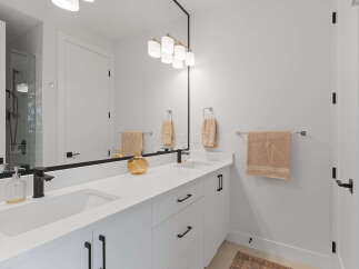 This modern bathroom features a sleek white double vanity with black hardware, complemented by a large frameless mirror reflecting the stylish light fixture above.