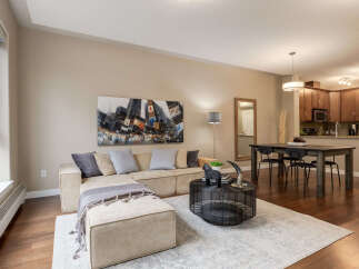 Experience modern urban living in this stylish condo featuring a spacious sectional sofa and a large cityscape artwork.