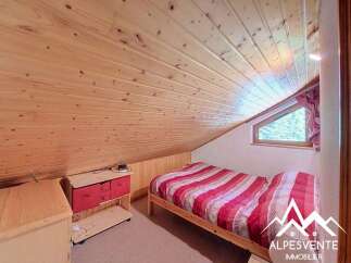 This charming attic bedroom features a cozy wooden ceiling and walls, creating a warm and inviting atmosphere.