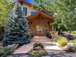 This stunning mountain home features a grand entrance with a covered porch, double wooden doors, and stone accents.