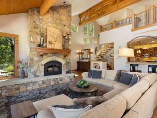 Experience rustic elegance in this stunning living room, featuring a grand floor-to-ceiling stone fireplace and exposed wooden beams that add warmth and character.