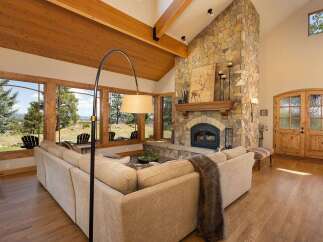 Experience breathtaking mountain views from this stunning living room, featuring a grand stone fireplace and vaulted wood-beamed ceilings.