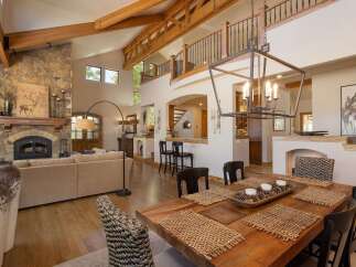 Experience rustic elegance in this spacious living and dining area, featuring a grand stone fireplace and soaring vaulted ceilings with exposed wooden beams.