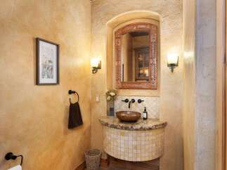 This charming powder room features a rustic aesthetic with textured ochre walls and a decorative tiled vanity.