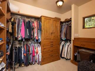 Discover ample storage in this spacious walk-in closet, featuring custom wooden shelving and a built-in dresser.