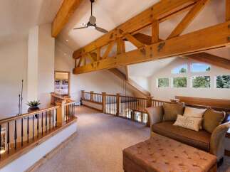 Experience rustic charm in this spacious loft area, featuring exposed wooden beams and a vaulted ceiling with a ceiling fan.