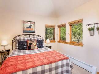 This charming bedroom features a cozy queen-size bed adorned with a playful black dog-themed pillow and a vibrant coral throw blanket.