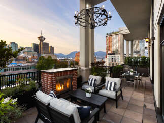 Experience luxury urban living with this stunning penthouse balcony, featuring a cozy brick fireplace and comfortable seating perfect for enjoying breathtaking city and mountain views.