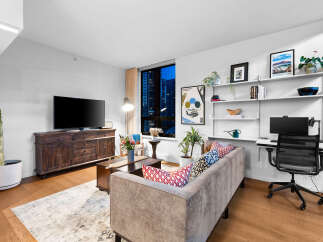 Experience modern urban living in this stylish apartment featuring a spacious living area with a large TV and a comfortable sofa adorned with decorative pillows.