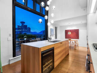 Experience modern luxury in this stunning kitchen featuring a sleek wooden island with a built-in wine fridge and marble countertops.
