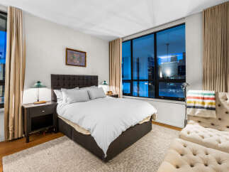 Experience urban living at its finest in this stunning bedroom featuring a luxurious king-sized bed and expansive windows offering breathtaking city views.