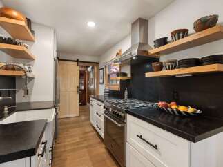 This modern kitchen boasts sleek black countertops and white cabinetry, complemented by open wooden shelving displaying decorative bowls and mugs.