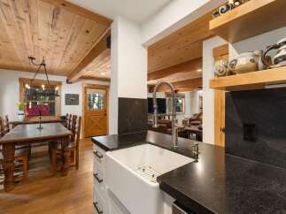 Experience rustic charm in this inviting dining area and kitchen, featuring a spacious wooden dining table with chairs and a modern farmhouse sink with a gooseneck faucet.