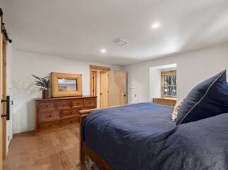 This charming bedroom features a rustic wooden dresser with a decorative mirror, complemented by a large, comfortable bed dressed in deep blue linens.