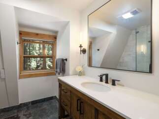 This modern bathroom features a rustic wooden vanity with black hardware, complemented by a sleek white countertop and undermount sink.