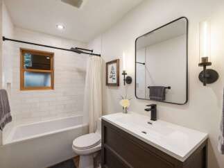 This modern bathroom features a sleek white subway tile shower and tub surround, complemented by a warm wooden window frame.