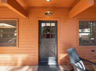 Step onto the charming porch of this cozy cabin, featuring a rustic Dutch door and warm orange siding.