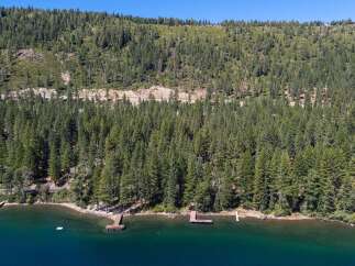 Experience serene lakeside living with this stunning aerial view of a property nestled amidst a lush pine forest.