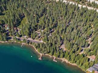 Experience the ultimate lakeside living with this stunning aerial view of a property nestled amongst tall pine trees.