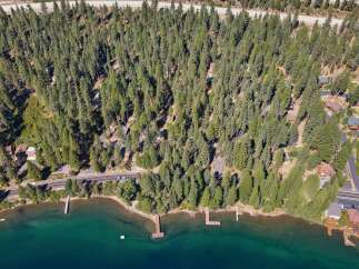 Experience serene lakeside living with this stunning aerial view of a property nestled amidst a dense pine forest.