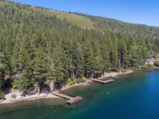 Experience lakeside living with this stunning aerial view of a property featuring multiple docks extending into the crystal-clear blue water.