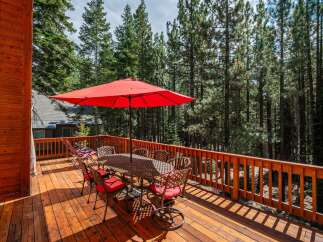 Enjoy outdoor dining and relaxation on this spacious wooden deck, complete with a large red umbrella and a dining set for six.