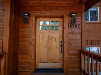 Welcome to this charming log cabin home, featuring a beautiful natural wood front door with a multi-pane glass insert and a rustic black handle.