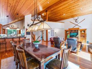 Experience rustic charm in this spacious dining and living area, featuring a grand wooden dining table perfect for gatherings and a cozy living space with a large TV and fireplace.