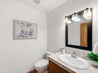 This stylish bathroom features a modern vanity with a sleek countertop and a white oval sink, complemented by a decorative light fixture above a large black-framed mirror.
