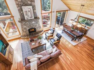 Experience rustic charm in this spacious living area featuring a grand stone fireplace and vaulted wood-paneled ceilings.