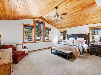 Experience rustic charm in this spacious bedroom, featuring a vaulted wood-paneled ceiling and large windows offering serene forest views.