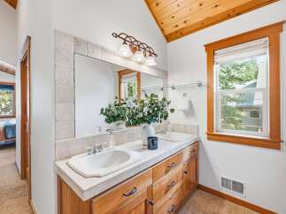 This charming bathroom features a spacious double vanity with ample storage and elegant stone tile accents around the large mirror.
