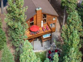 Experience ultimate relaxation in this stunning mountain retreat, featuring a spacious wooden deck with a hot tub and ample seating for outdoor entertaining.